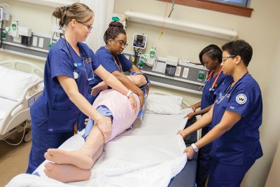 A group of diverse female nursing students practice in the simulation center.