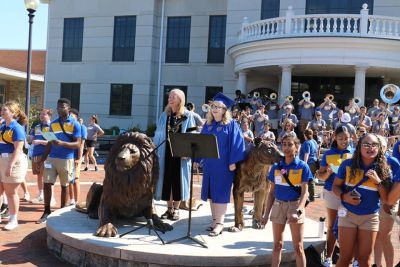 President Robertson stands at the Pride statue in regalia with student leaders during the 2022 academic convocation.