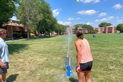 A female student launches a homemade bottle rocket across Memorial Field.