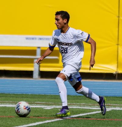 Hector Suriel, in white Widener uniform, kicking a soccer ball