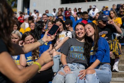 Someone taking a photo of two Widener students sitting in the stands at homecoming