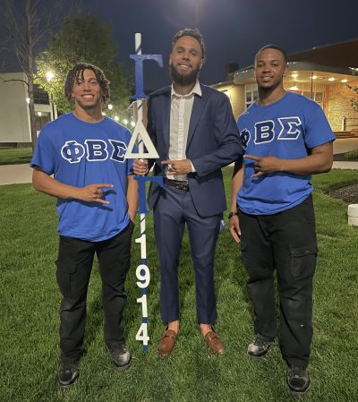 Three members of the Phi Beta Sigma Fraternity stand with a pole of their letters
