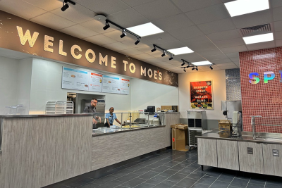 The newly renovated Moe's counter with "Welcome to Moe's" across the top and workers behind the counter setting up