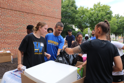 Volunteers helping students and families unload a cart of items outside of a residence hall