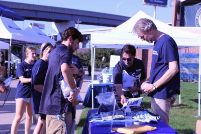 Students gather around a table outdoors as faculty pass out materials 