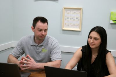 Two people sit at laptops, working together.