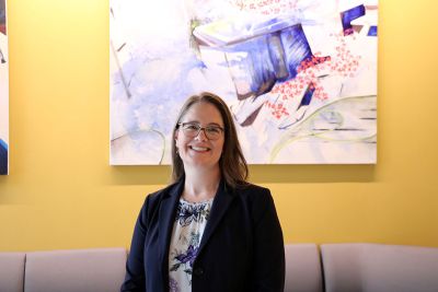 Lisa Grimm poses, smiling at the camera with an abstract painting on the wall behind her