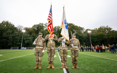 Four ROTC cadets in army fatigues are lined up, one holds the American Flag