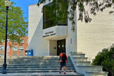 A student walks up the front steps of Wolfgram Memorial Library on a sunny day