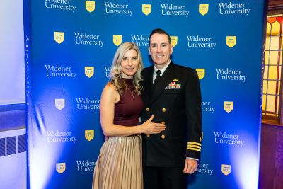 Patricia Duff and Jason Duff, in Navy uniform, standing in front of a blue Widener backdrop