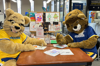 Chester and Melrose mascots coloring at a table in the library