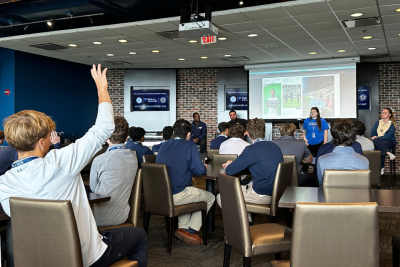 A student raises their hand with a question at a presentation.