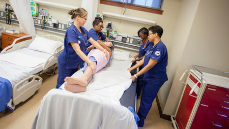 Four accelerated nursing nursing students in lab working with mannequin
