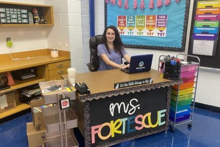 Teacher sits at desk in elementary school classroom