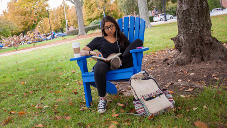 Student reading in adirondack chair in fall