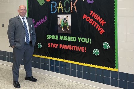 Education doctoral graduate Mike Kelly standing next to a bulletin board in a school