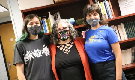 Two students stand with a professor in front of a book shelf