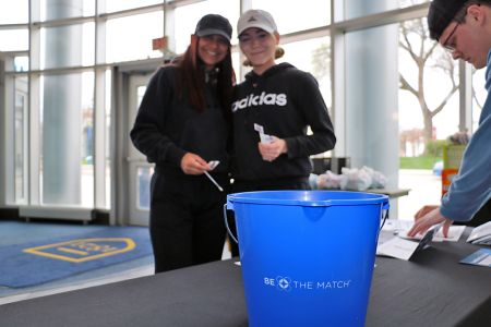 Two students hold bone marrow swab sticks, with a blue bucket in the foreground