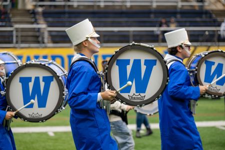 Three members of the marching band drumline playing on the field