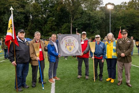 Seven people on the football field, with the center two holding a framed drumhead