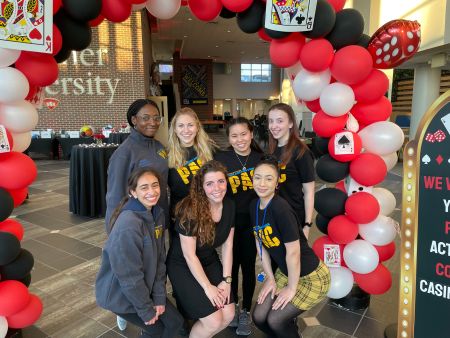 Seven students pose in the University Center Atrium surrounded by red, white, and black balloons
