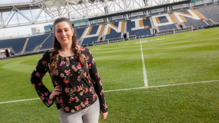 A Widener University student who interns with the Philadelphia Union stands in front of the soccer field.
