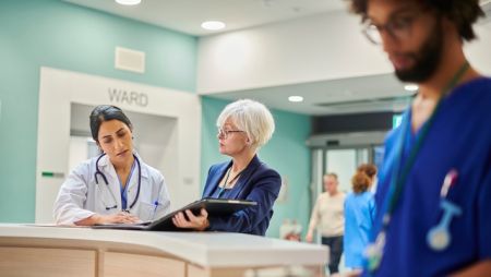 Two nurses leaders having a conversation while looking at a binder. A third nurse is in the foreground.
