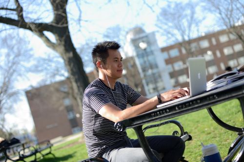 Student studying on laptop, sitting outside at a picnic table