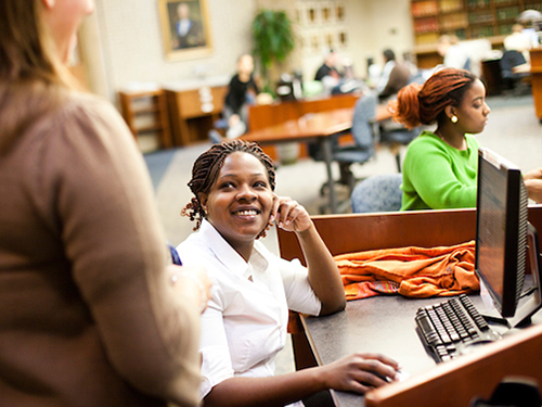 Student in library on computer 500x375 Student in library on computer and talking to another student