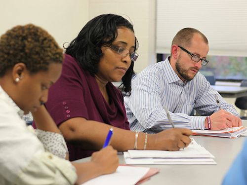 Three adult students taking notes in class