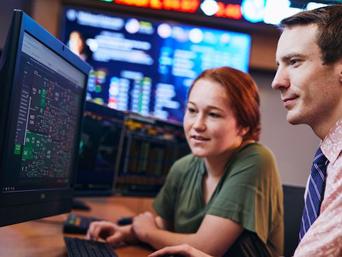 Finance Lab 500x375 students work together in finance lab with stock ticker in background