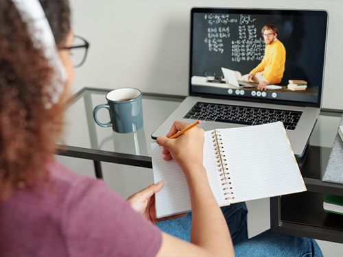 Student writing in notebook with laptop