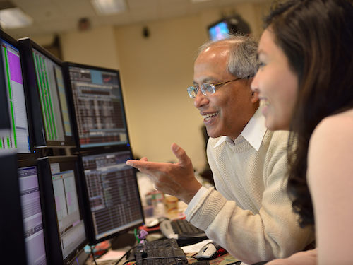 Data analytics student and professor reviewing data on multiple computer monitors