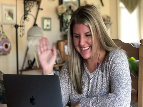 Student Samantha Begley, member of a Personal Student Success Team, waves to people on a laptop