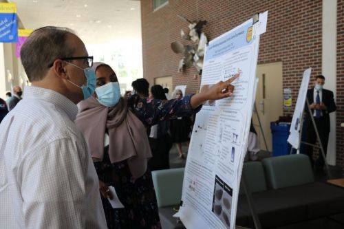 A female student engages with a guest at the SURCA Symposium while presenting their research.