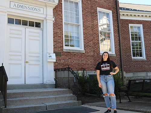 Chloe Mingioni stands outside Muller Hall, with an Admissions sign over the door.