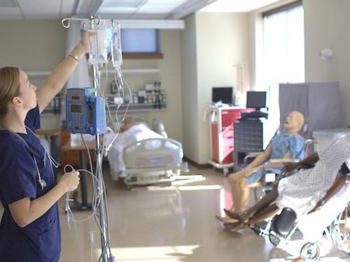 A woman nursing student in scrubs hangs a bag onto an IV pole in Widener's nursing simulation lab.