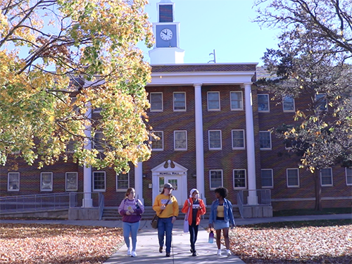 Four students walking away from Howell Hall on a fall day