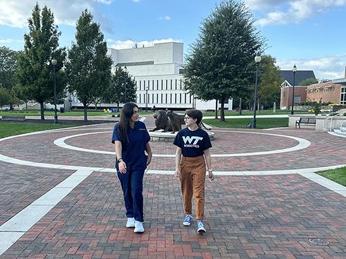 Two students walking on campus near the Pride statues