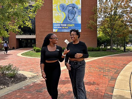 Two siblings walk on campus talking and laughing