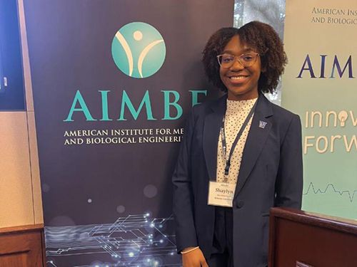 Shaylyn Westmoreland smiles for a photo in front of a sign at an industry research conference