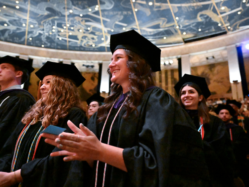 Graduates smile and clap during their commencement ceremony