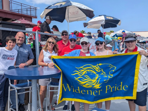 Alumni pose with a "Widener Pride" flag at the baseball game