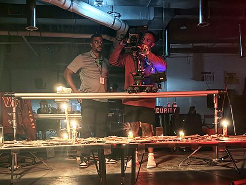 Two men work behind the scenes on a film production, with one holding a camera
