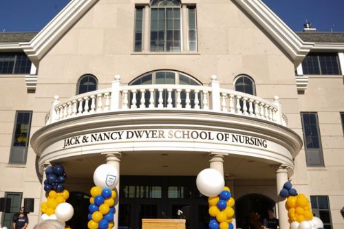 The outside of Founders Hall reading the name "Jack &amp; Nancy Dwyer School of Nursing". There are blue, yellow and white balloons outside of the building entrance.