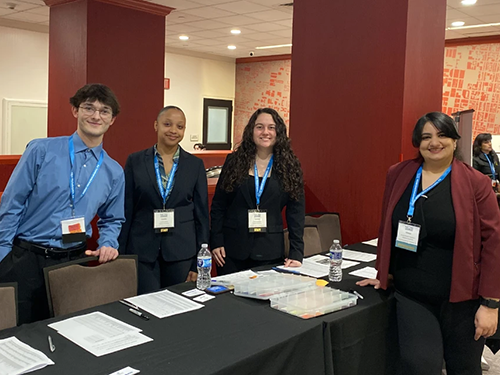 Three business students and a professor standing at a long table at a professional conference
