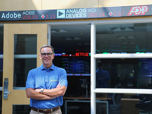 Business Dean Cary Caro stands in front of the Finance Lab with a stock ticker above him