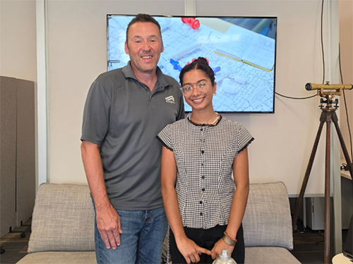 Lou Rodriguez and Anmona Das stand next to each other in front of a TV screen and couch
