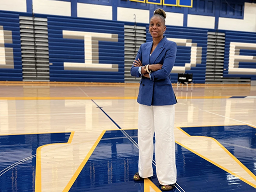 Crystal Gibson stands in the center of the basketball court, wearing blue blazer and white pants