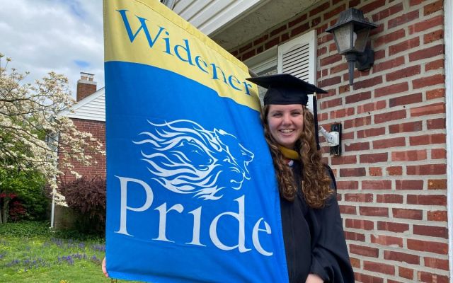 widener graduate in cap and gown with widener pride flag